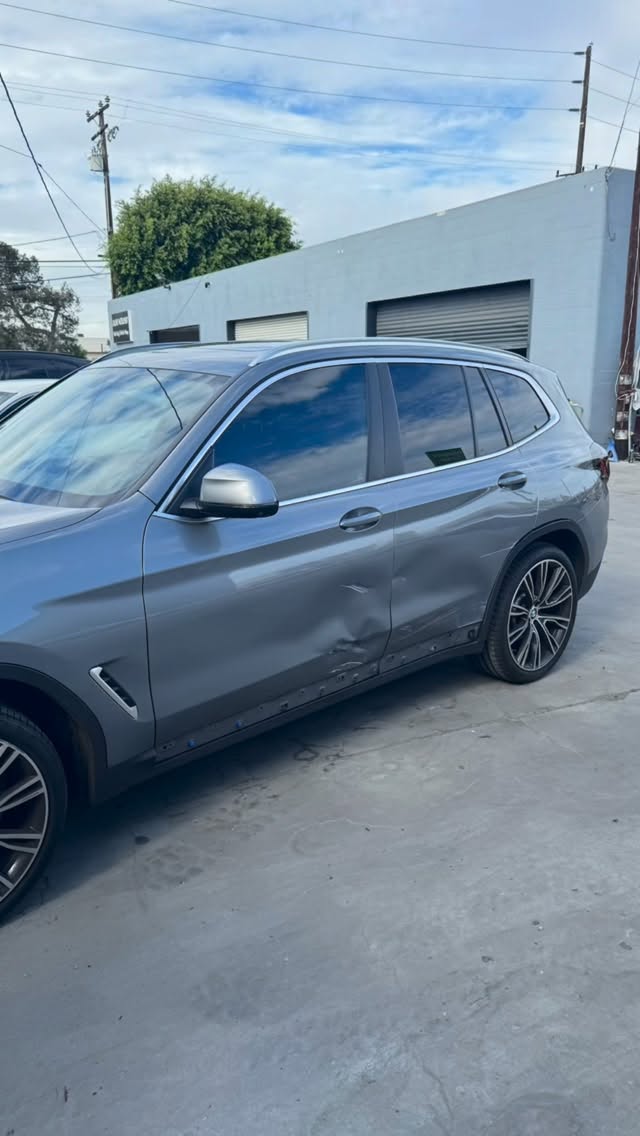 Gray BMW SUV with visible driver-side exterior damage outside the Calibri Motorsport shop