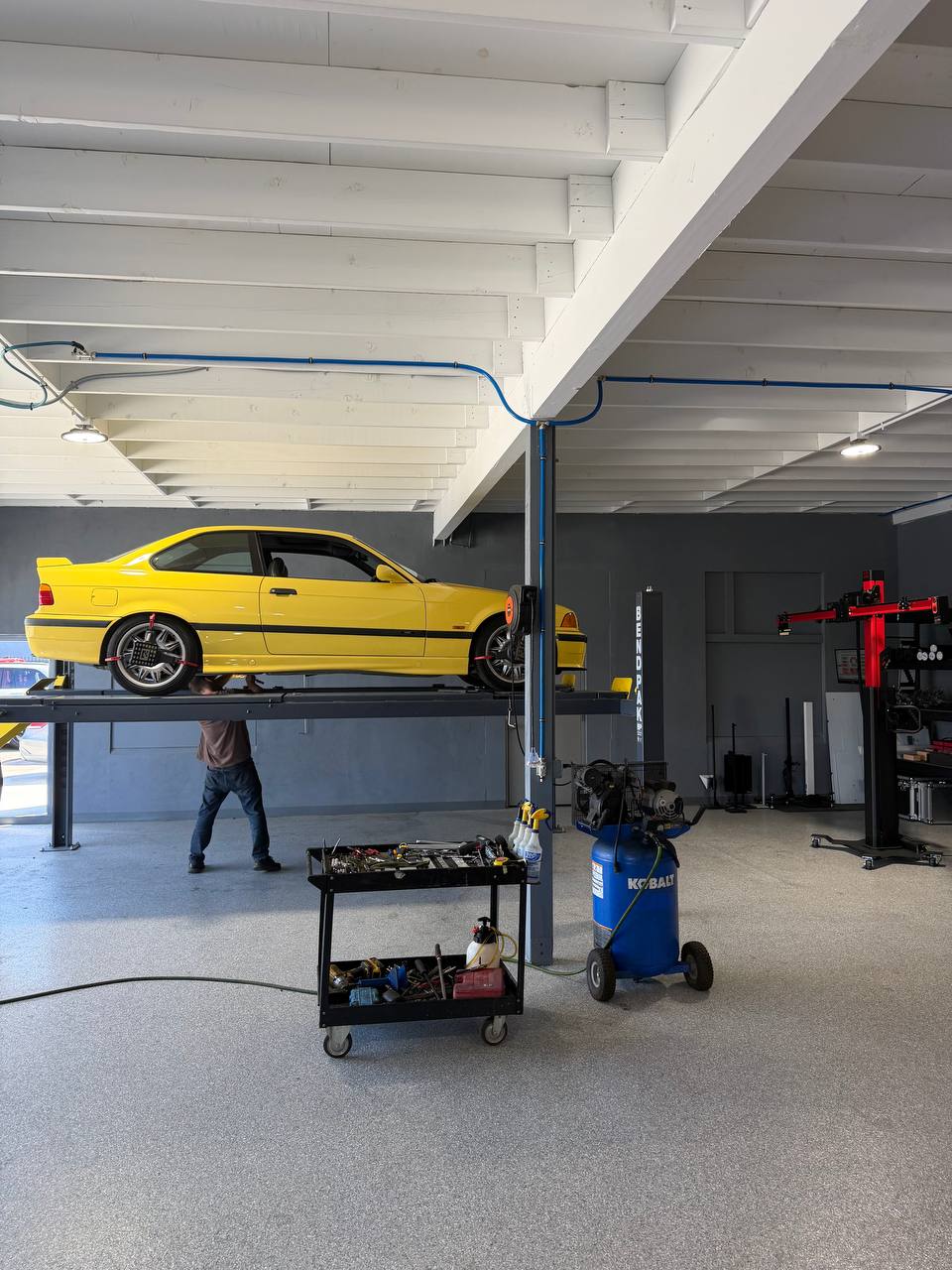 Side view of a yellow BMW E36 M3 elevated during alignment inspection