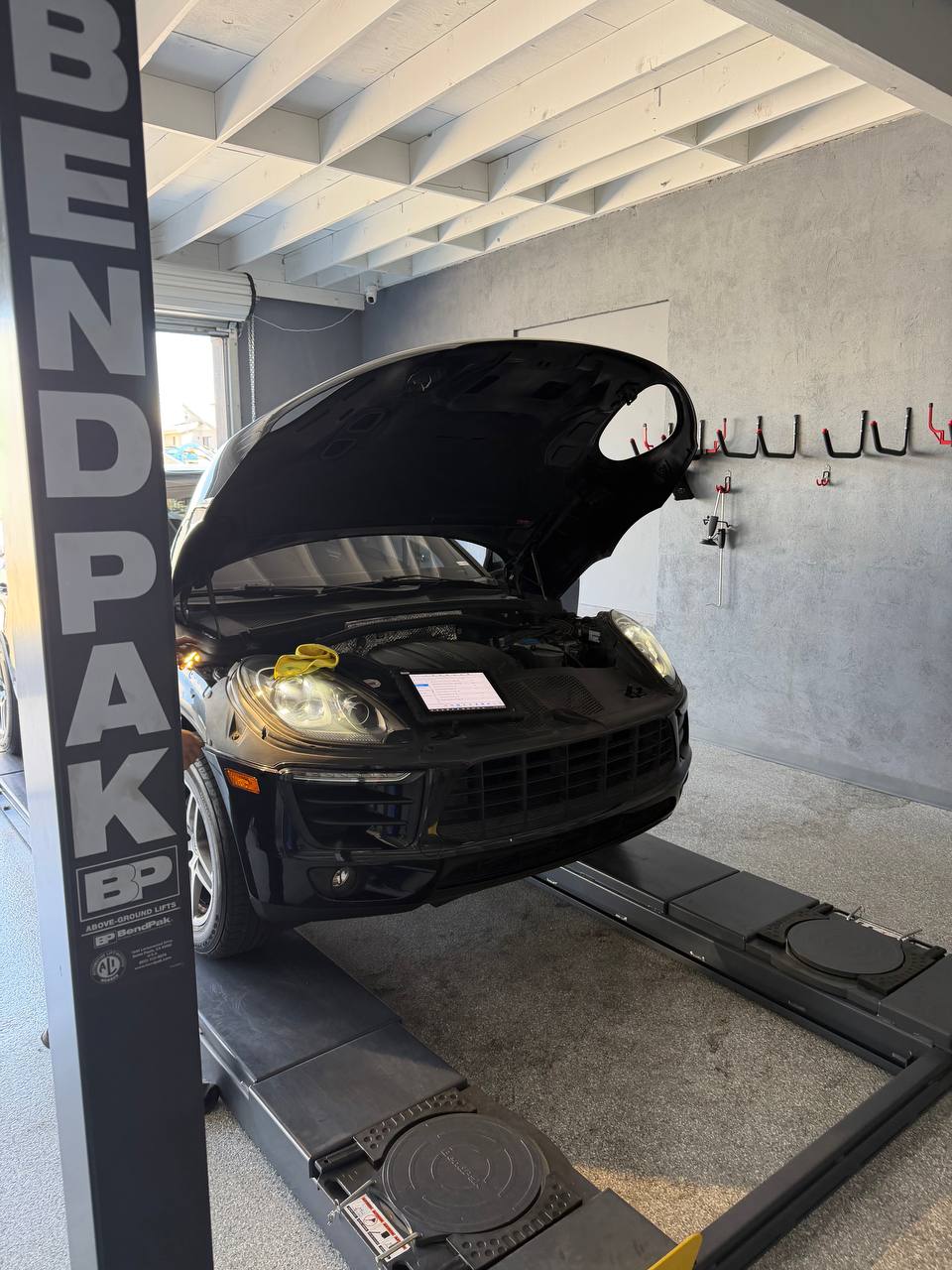 Black Porsche Macan in the service bay with its hood open during diagnosis