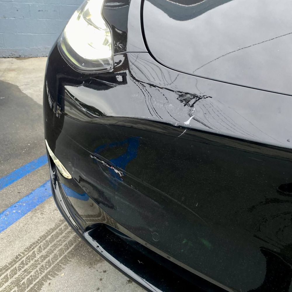 Close view of visible damage on the corner of a black Tesla bumper