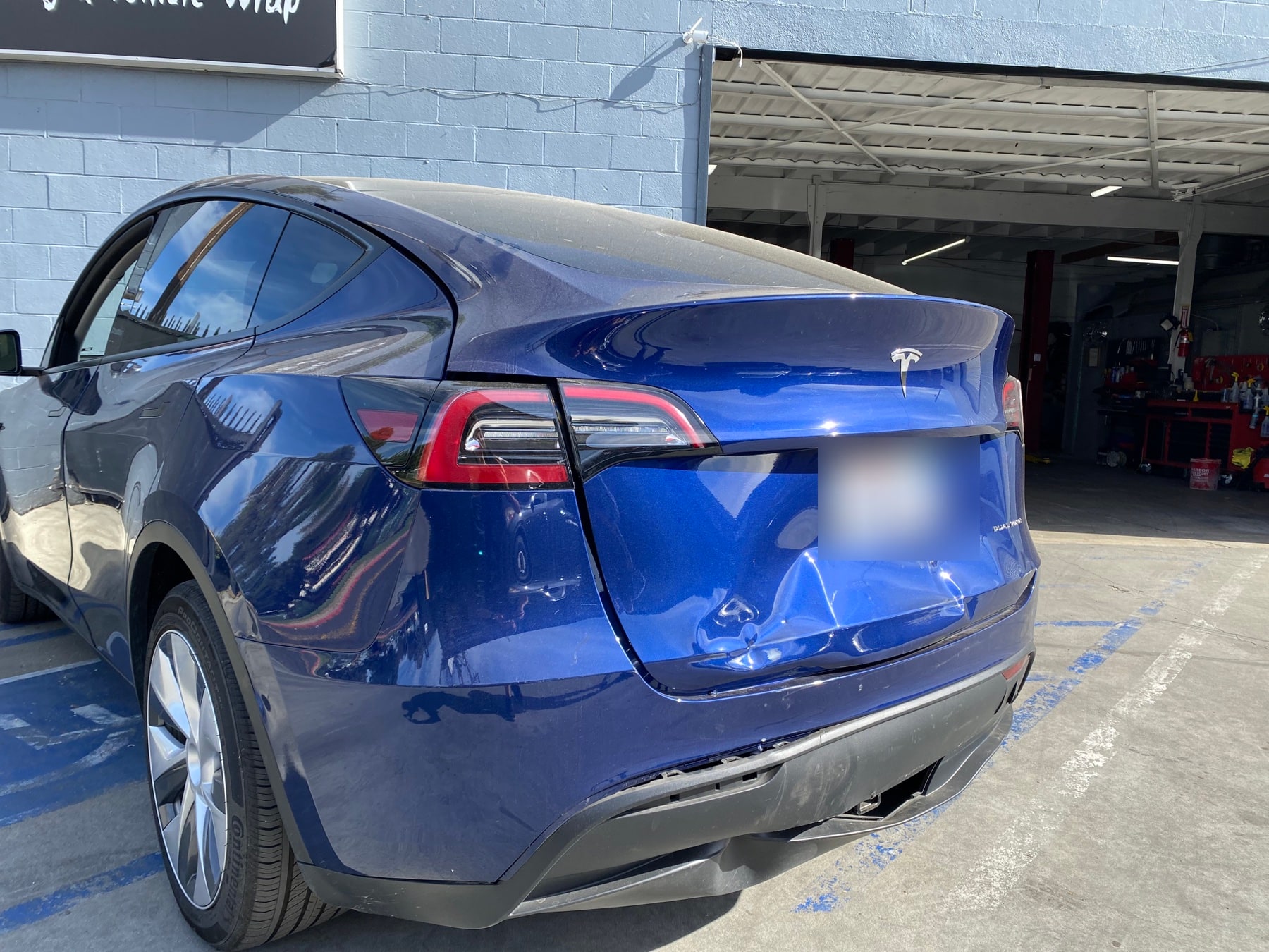 Rear collision damage on a blue Tesla Model Y before repair