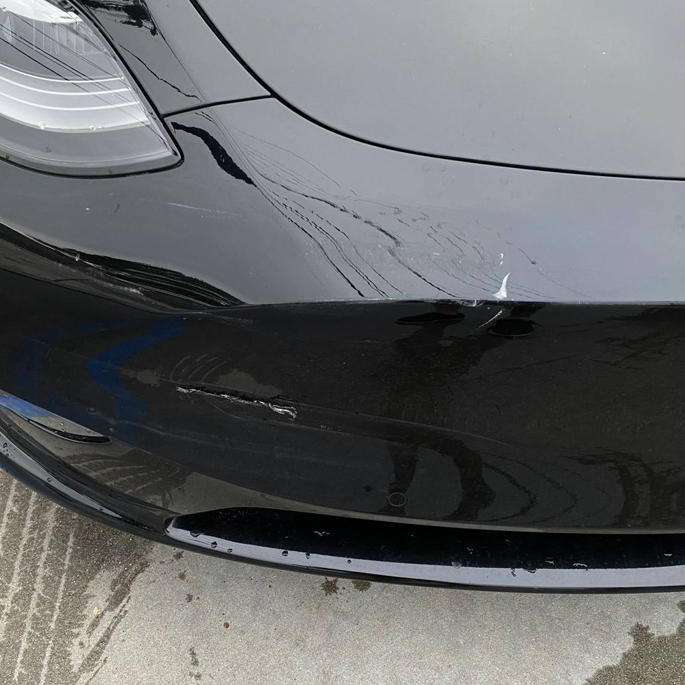 Close view of front bumper collision damage on a black Tesla Model Y