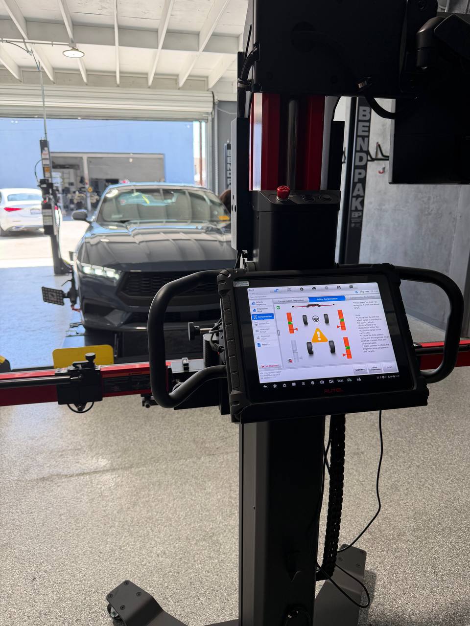 Ford Mustang on an alignment rack with initial measurements shown on the display