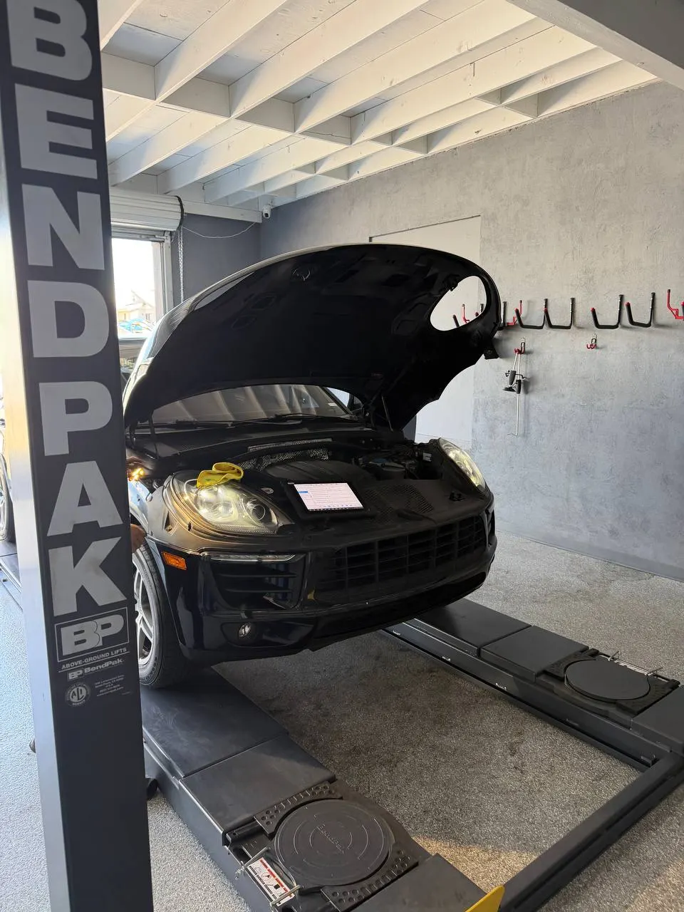 Black Porsche Macan in the service bay with its hood open during diagnosis