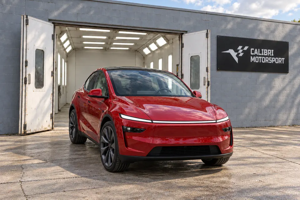 Red refreshed Tesla Model Y outside a paint booth built into the gray shop facade, with Calibri Motorsport signage