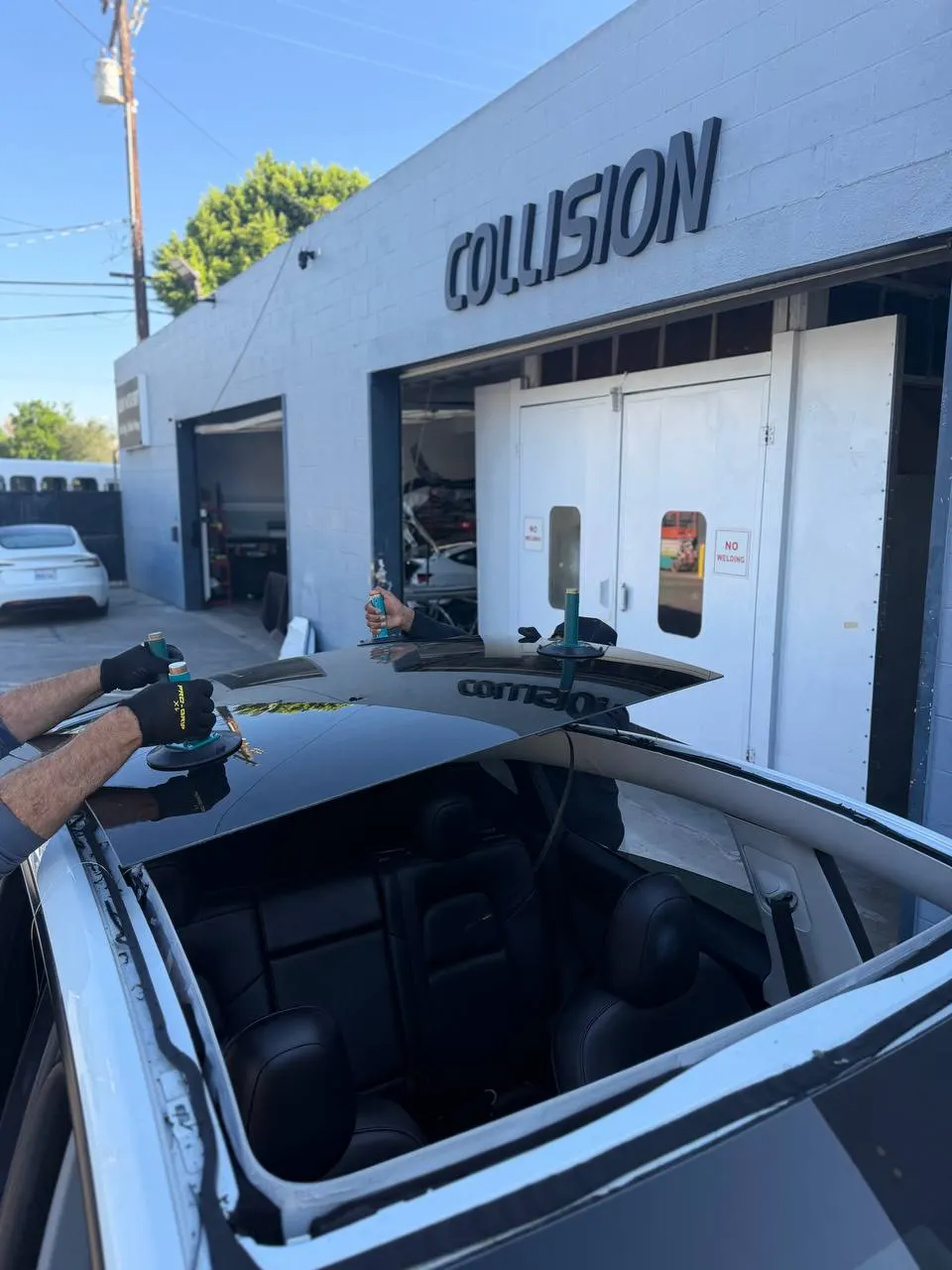 Exposed roof opening and suction-supported glass during work on a white Tesla Model Y.