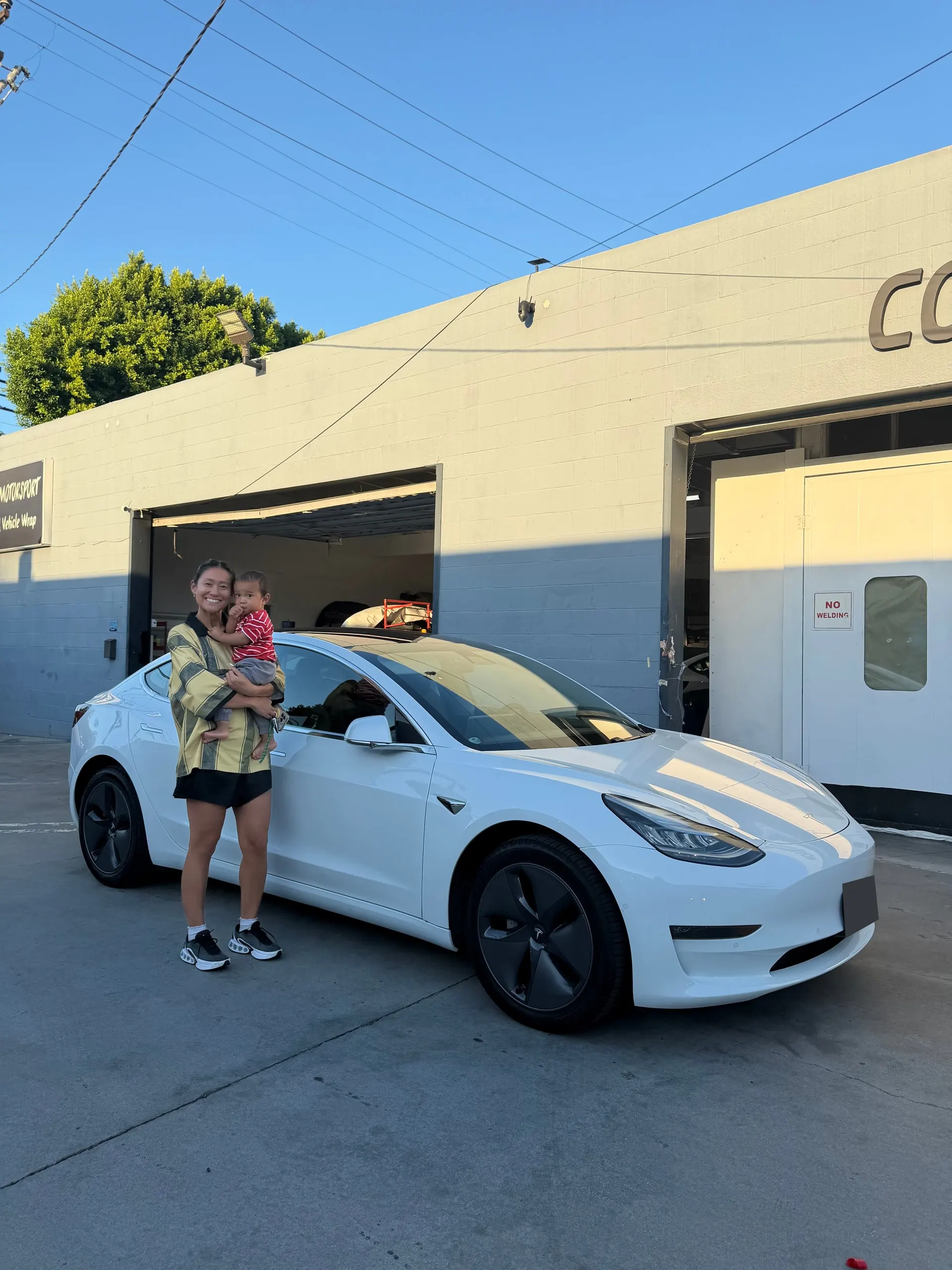 Customer with a child beside a white Tesla outside the Calibri Motorsport workshop