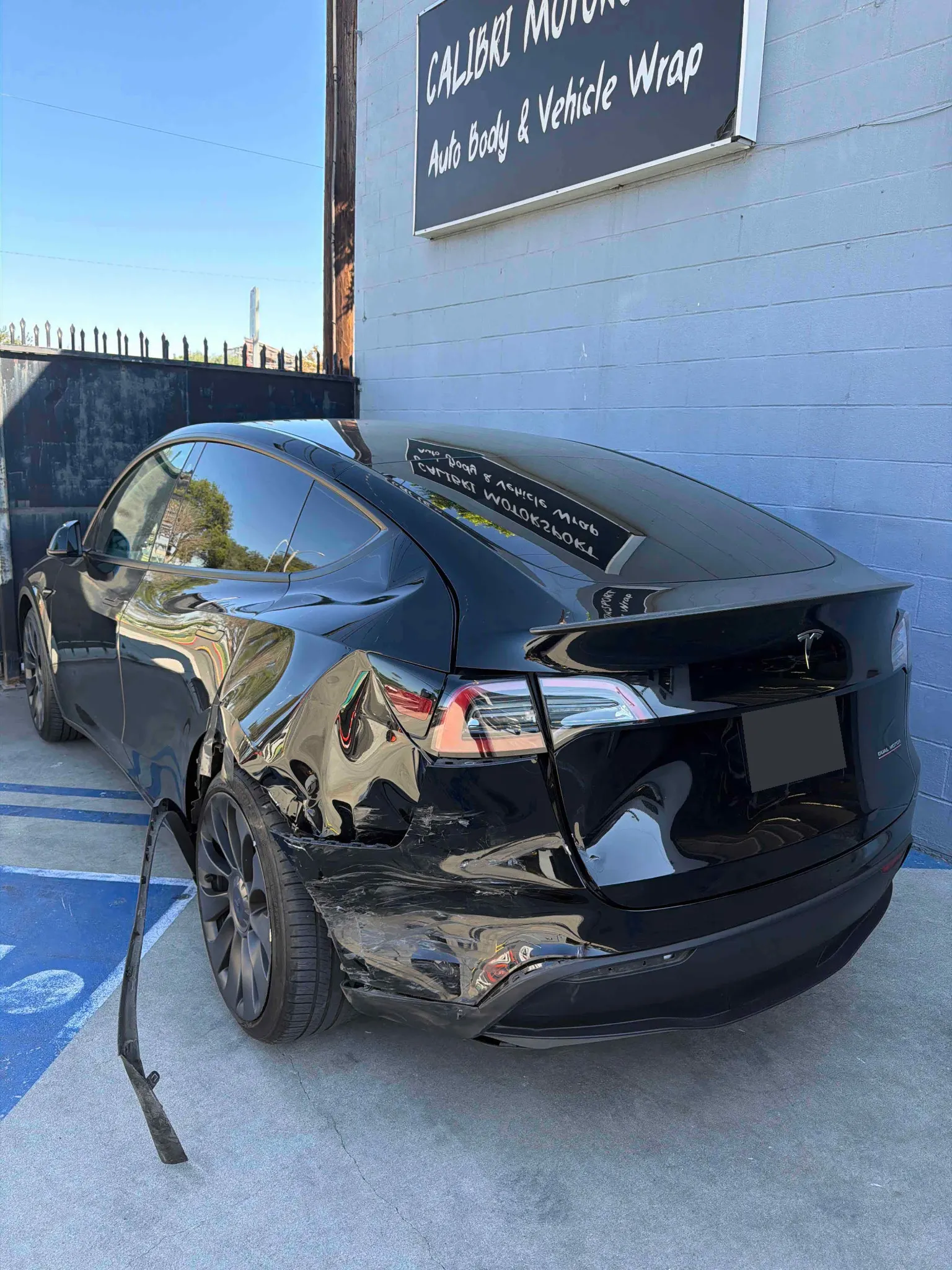 Tesla with visible rear collision damage beside the Calibri Motorsport shop sign