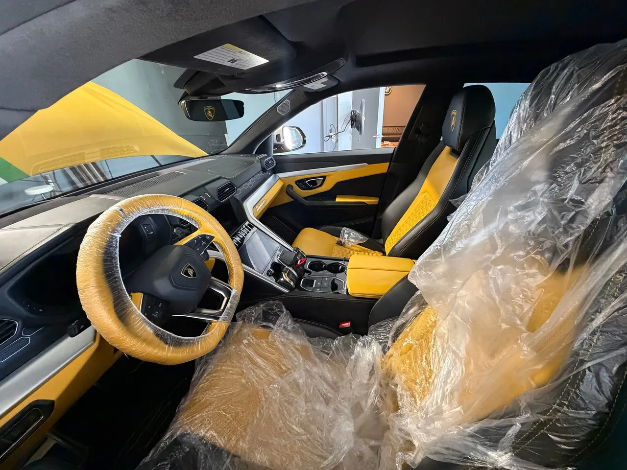 Yellow and black Lamborghini Urus interior with protective covering on the driver’s seat and steering wheel