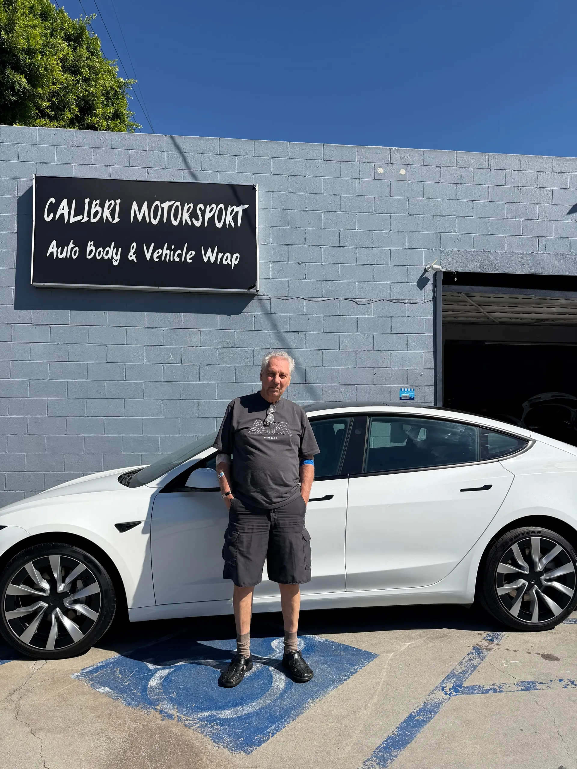 Customer beside a white Tesla beneath the Calibri Motorsport workshop sign