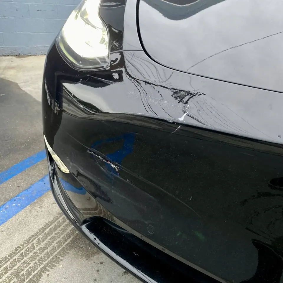 Visible front bumper damage on a black Tesla Model Y before collision work