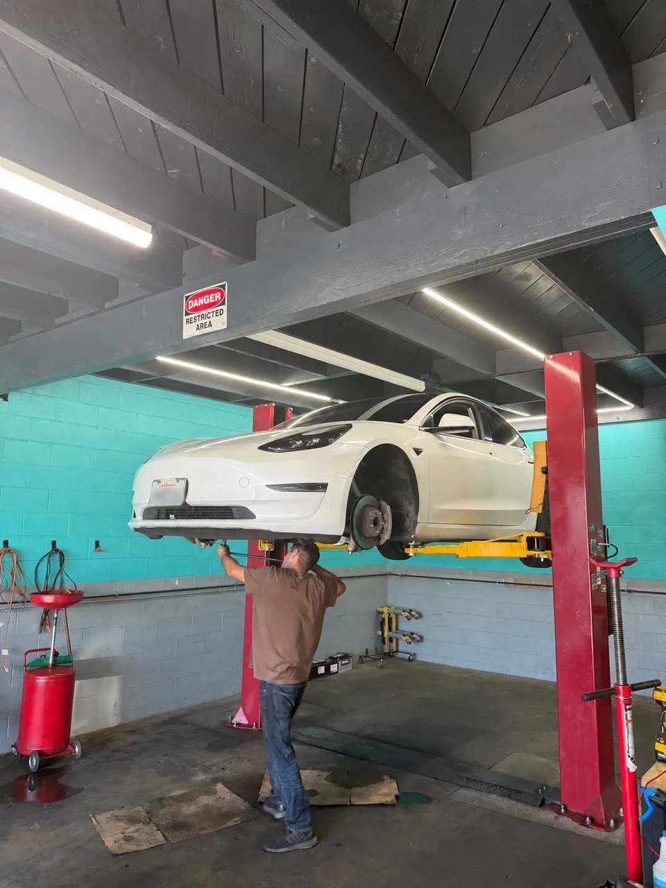 Technician working beneath a Tesla Model 3 on a lift at Calibri Motorsport