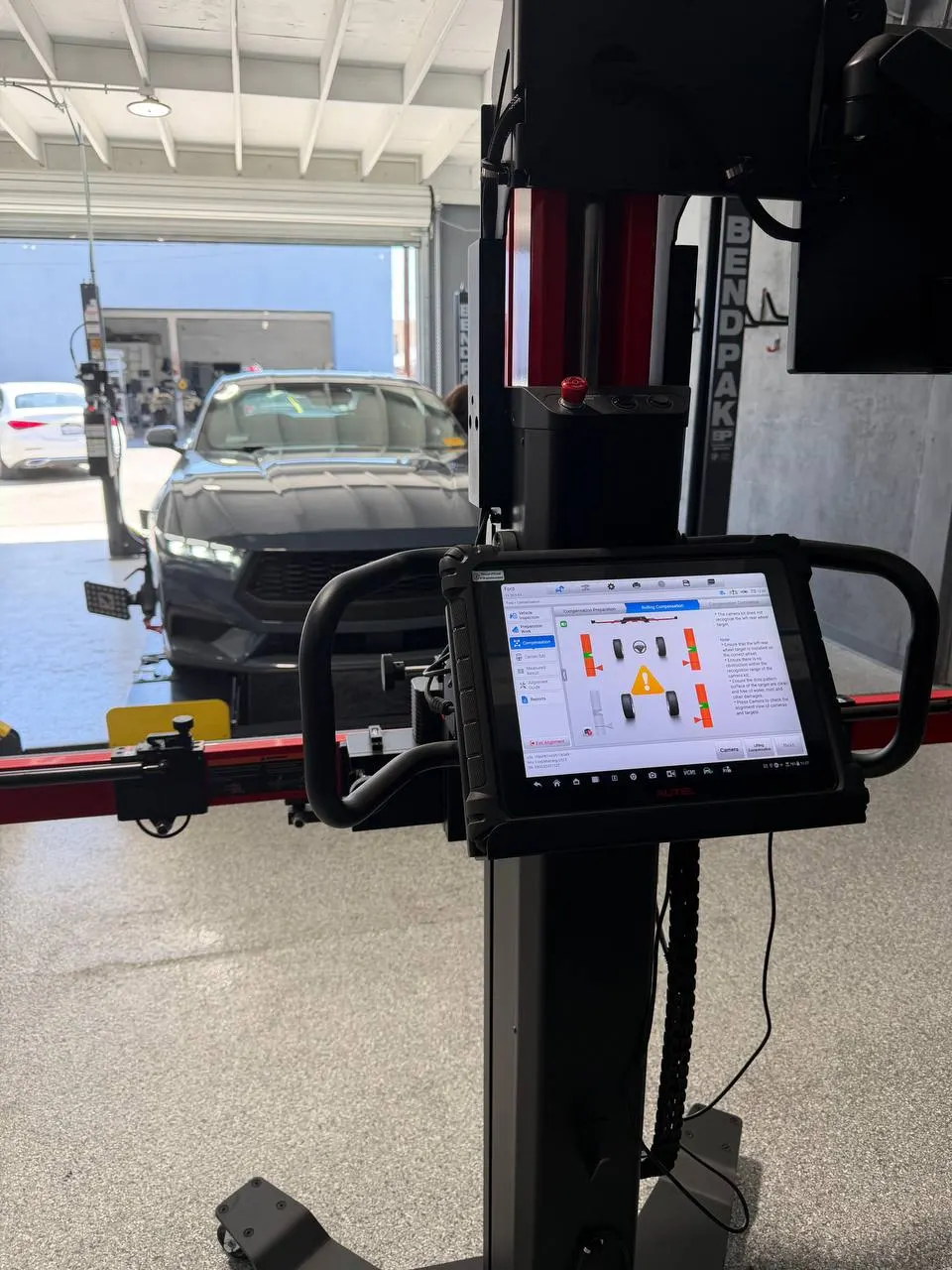 Ford Mustang on an alignment rack with the rolling-compensation setup screen on the tablet