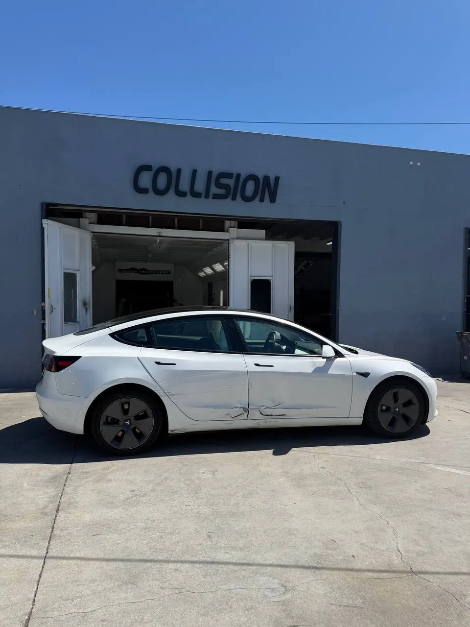 Original shop photograph of Tesla Model 3 damage across both driver-side doors before repair